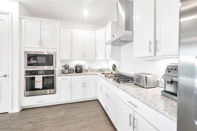 kitchen with light hardwood / wood-style floors, wall chimney range hood, stainless steel appliances, and white cabinets