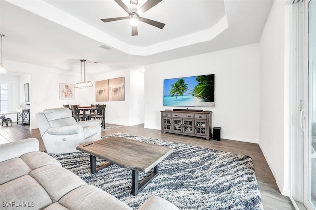 living room with wood-type flooring, a tray ceiling, and ceiling fan