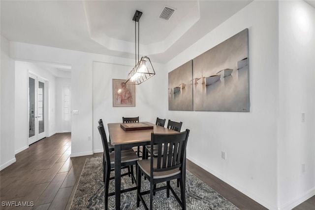 dining area with a raised ceiling, dark wood-type flooring, and french doors