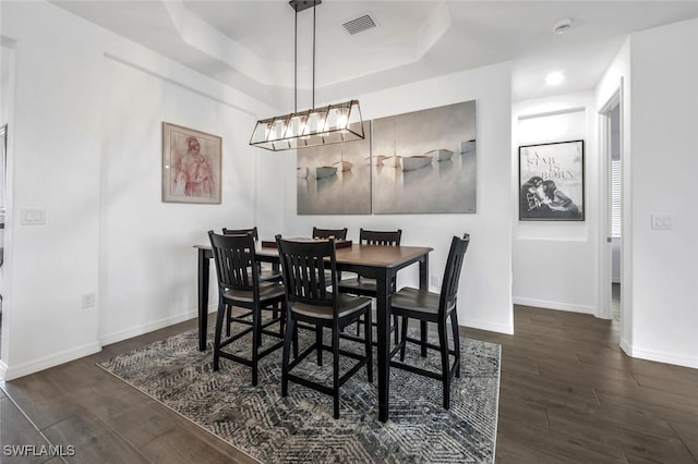 dining area featuring an inviting chandelier, a raised ceiling, and dark hardwood / wood-style floors