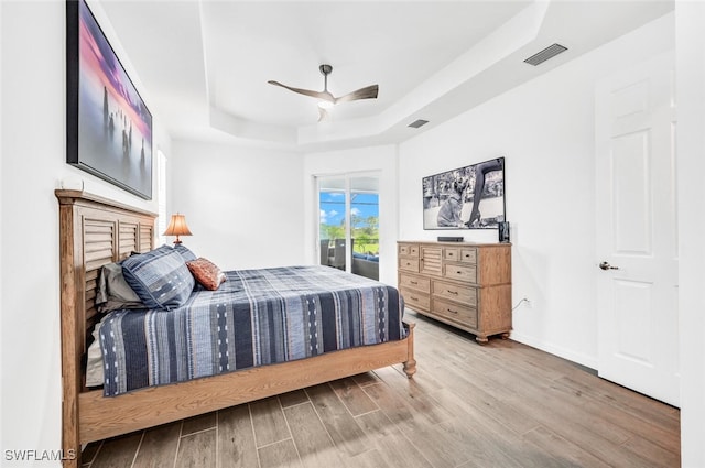 bedroom with access to outside, a tray ceiling, ceiling fan, and hardwood / wood-style flooring