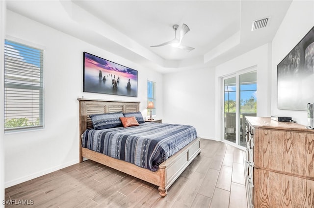 bedroom with light hardwood / wood-style floors, a tray ceiling, ceiling fan, and access to exterior