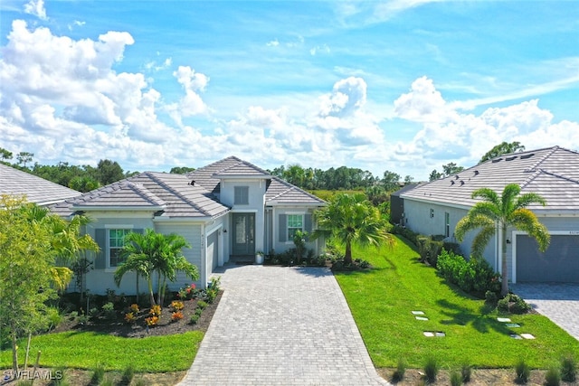 ranch-style home featuring a garage, decorative driveway, a front yard, a tile roof, and stucco siding