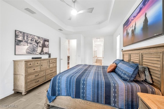 bedroom with a raised ceiling, light wood-type flooring, connected bathroom, baseboards, and a ceiling fan