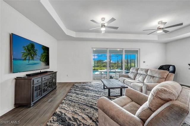 living room with a tray ceiling, dark wood-style floors, a ceiling fan, and baseboards