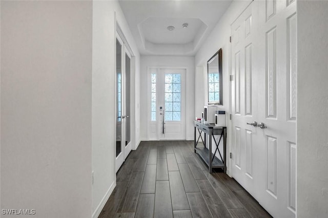 hall with a tray ceiling, wood tiled floors, and baseboards