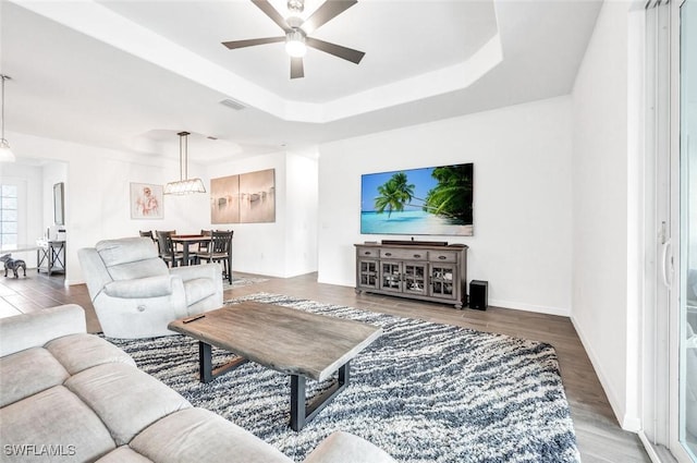 living area with ceiling fan, wood finished floors, a tray ceiling, and baseboards