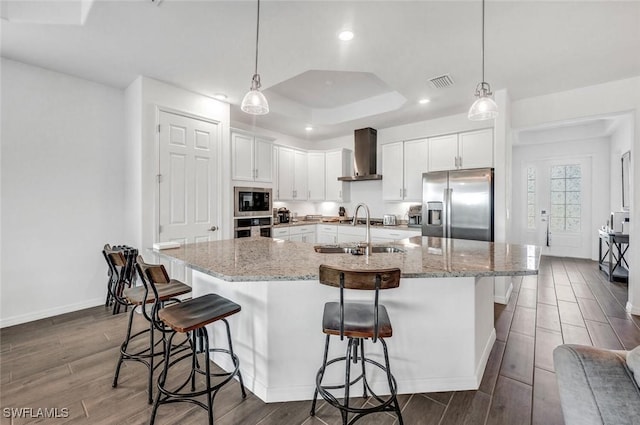 kitchen with appliances with stainless steel finishes, wall chimney range hood, a sink, wood finish floors, and white cabinetry
