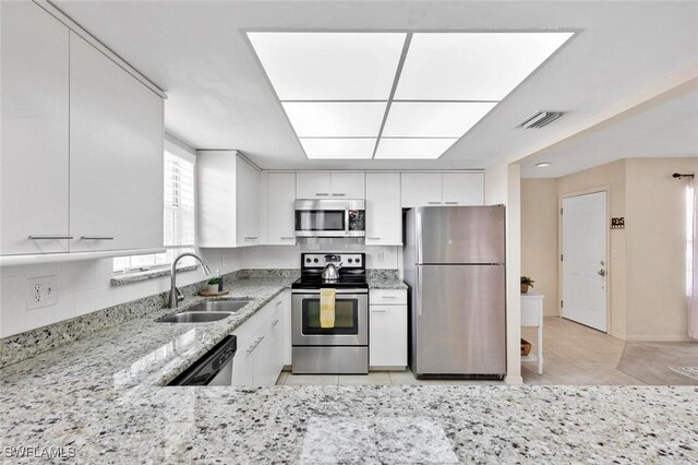 kitchen featuring appliances with stainless steel finishes, white cabinetry, light stone counters, light tile patterned floors, and sink