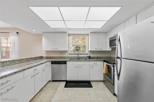 kitchen featuring white cabinetry, light stone countertops, light tile patterned floors, stainless steel appliances, and sink