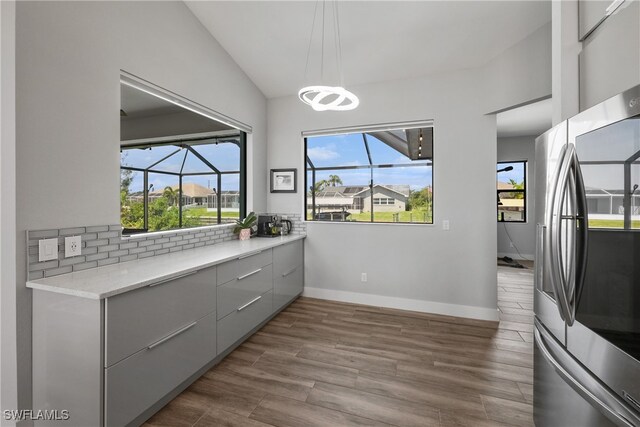 kitchen with decorative backsplash, stainless steel refrigerator with ice dispenser, light wood-type flooring, gray cabinets, and lofted ceiling