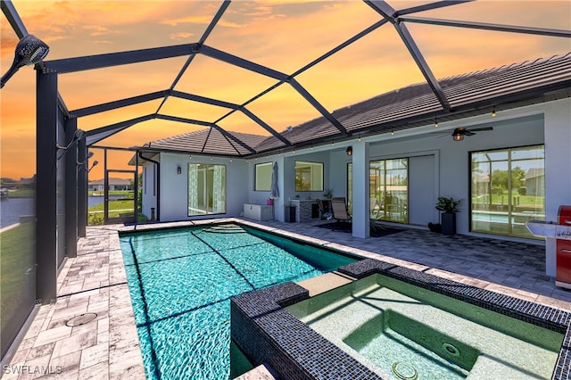 pool at dusk featuring ceiling fan, a lanai, a patio, and an in ground hot tub