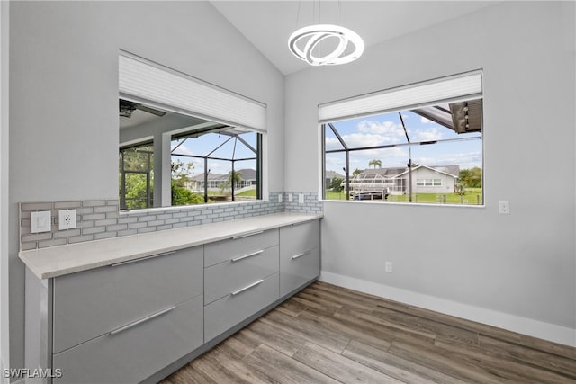 interior space featuring hardwood / wood-style floors, decorative backsplash, lofted ceiling, and a notable chandelier