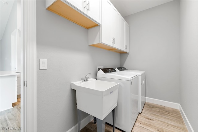 laundry area with light wood-type flooring, sink, washer and dryer, and cabinets