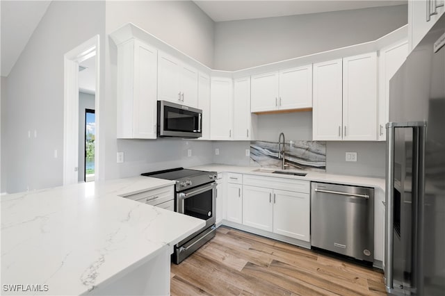 kitchen featuring white cabinets, sink, vaulted ceiling, stainless steel appliances, and light hardwood / wood-style floors