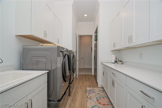 laundry area featuring light hardwood / wood-style flooring, cabinets, ornamental molding, sink, and washer and dryer