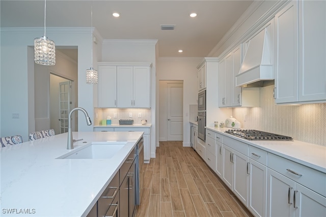 kitchen featuring appliances with stainless steel finishes, white cabinetry, pendant lighting, premium range hood, and sink