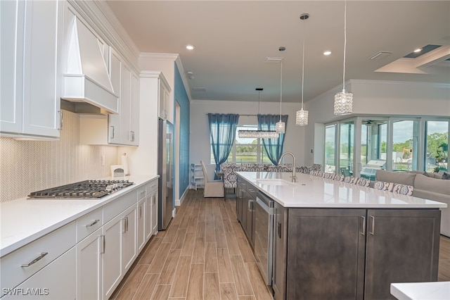 kitchen with white cabinets, premium range hood, pendant lighting, sink, and appliances with stainless steel finishes