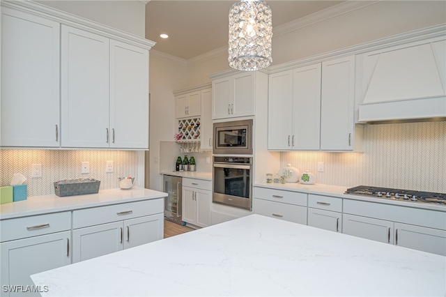 kitchen with hanging light fixtures, white cabinetry, stainless steel appliances, crown molding, and beverage cooler