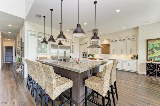 kitchen with appliances with stainless steel finishes, a large island with sink, dark hardwood / wood-style flooring, and pendant lighting