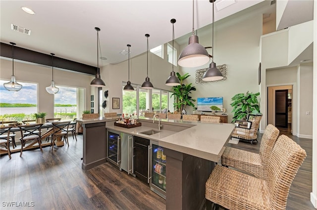 kitchen with an island with sink, sink, decorative light fixtures, a high ceiling, and dark hardwood / wood-style flooring