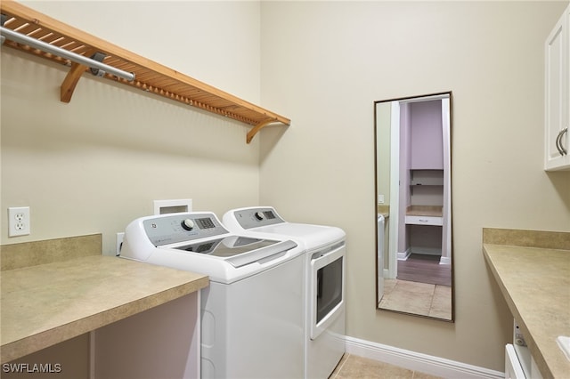 clothes washing area featuring separate washer and dryer, light tile patterned floors, and cabinets