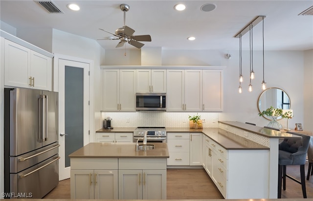 kitchen featuring pendant lighting, white cabinetry, high end appliances, and a kitchen island with sink