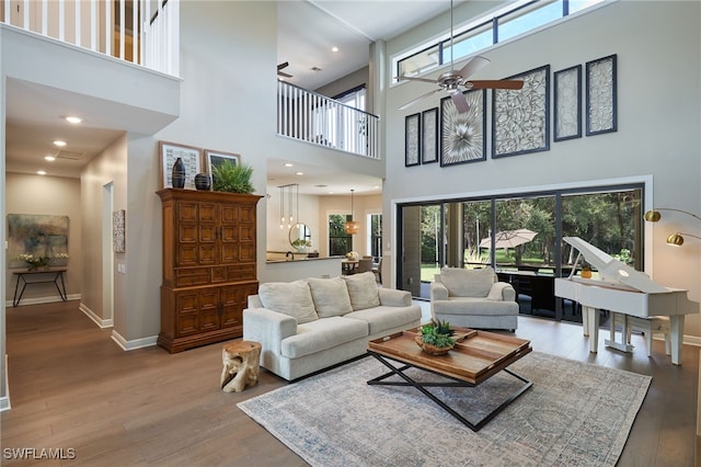 living room with a towering ceiling, ceiling fan, wood-type flooring, and a healthy amount of sunlight