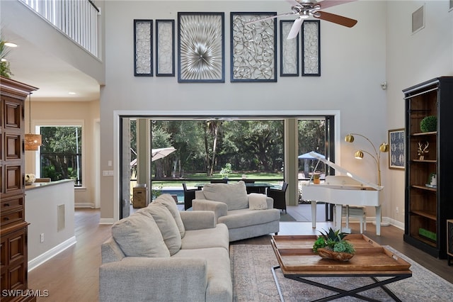 living room with a towering ceiling, hardwood / wood-style flooring, and ceiling fan