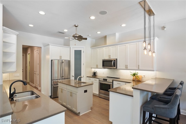 kitchen featuring white cabinetry, sink, stainless steel appliances, kitchen peninsula, and decorative light fixtures