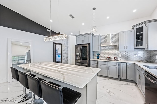 kitchen with pendant lighting, lofted ceiling, wall chimney exhaust hood, appliances with stainless steel finishes, and a kitchen bar