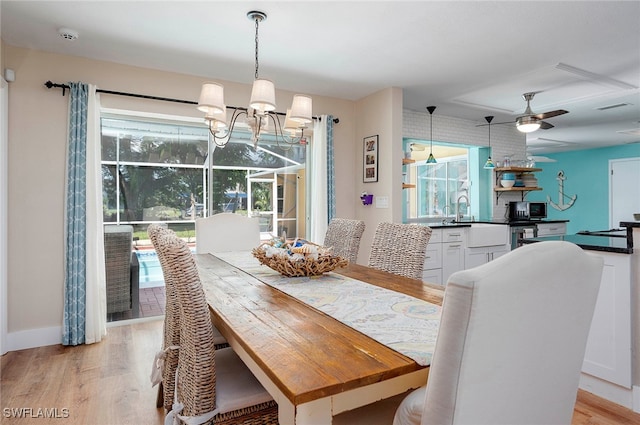 dining area with light wood-type flooring, ceiling fan with notable chandelier, and a wealth of natural light