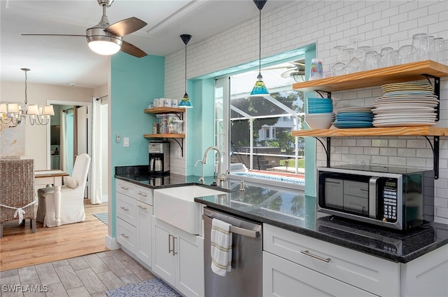 kitchen with white cabinets, ceiling fan with notable chandelier, stainless steel appliances, light hardwood / wood-style flooring, and dark stone counters