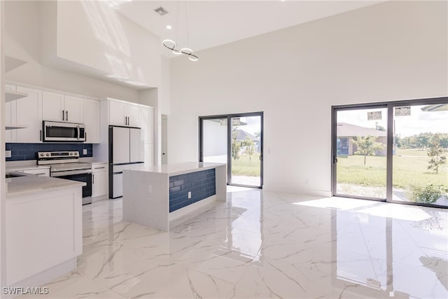 kitchen featuring white cabinetry, tasteful backsplash, stainless steel appliances, a high ceiling, and a center island