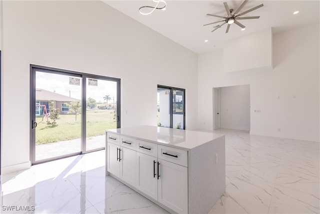 kitchen featuring ceiling fan, a center island, a high ceiling, and white cabinetry