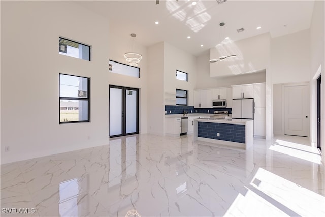 kitchen with a center island, white cabinetry, hanging light fixtures, stainless steel appliances, and a towering ceiling