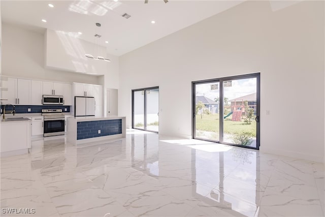 kitchen featuring hanging light fixtures, sink, white cabinetry, stainless steel appliances, and a towering ceiling