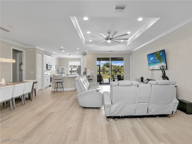 living room with ceiling fan, light hardwood / wood-style flooring, a raised ceiling, and ornamental molding