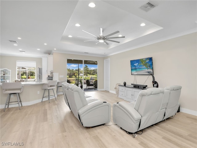 living room with light wood-type flooring, a raised ceiling, ornamental molding, and ceiling fan