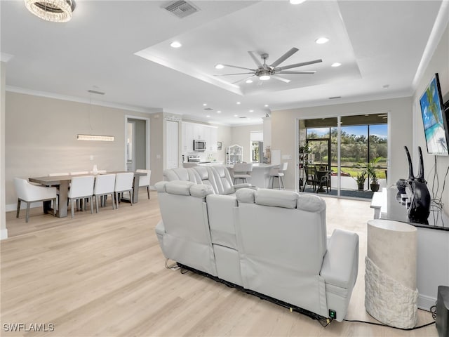 living room with ceiling fan, ornamental molding, light hardwood / wood-style flooring, and a tray ceiling