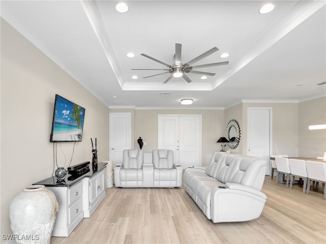 living room with ceiling fan, a raised ceiling, ornamental molding, and light hardwood / wood-style flooring