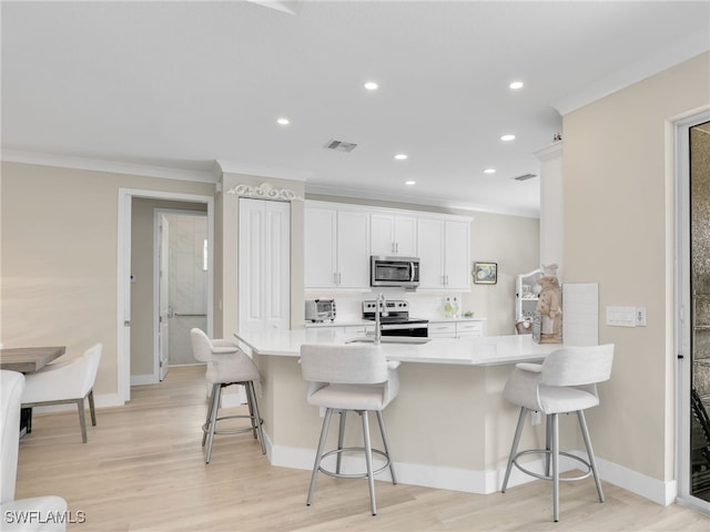 kitchen with light hardwood / wood-style flooring, stainless steel appliances, white cabinets, and a breakfast bar area