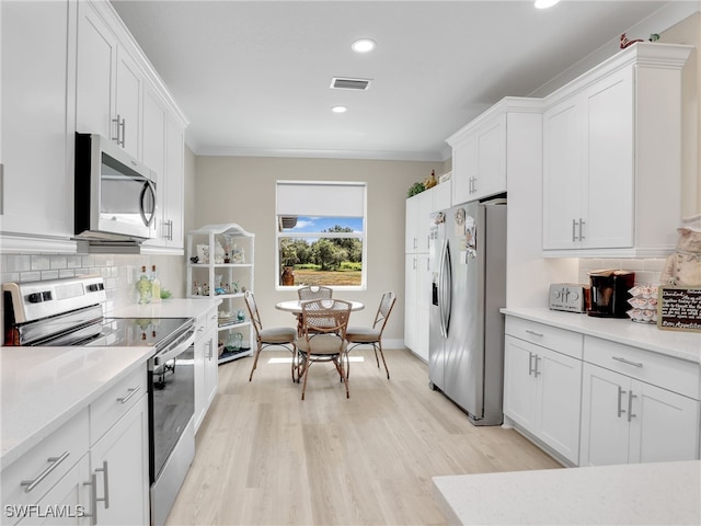 kitchen with white cabinets, ornamental molding, backsplash, stainless steel appliances, and light hardwood / wood-style floors