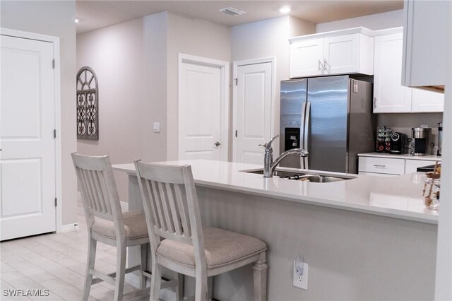 kitchen with kitchen peninsula, sink, stainless steel fridge with ice dispenser, white cabinetry, and a breakfast bar area