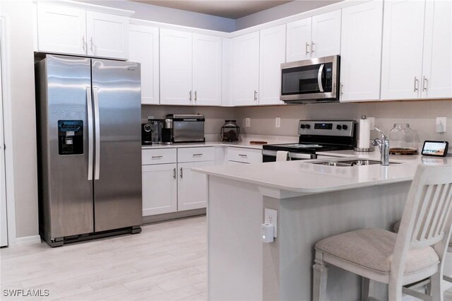 kitchen featuring light wood-type flooring, sink, white cabinetry, a kitchen bar, and appliances with stainless steel finishes