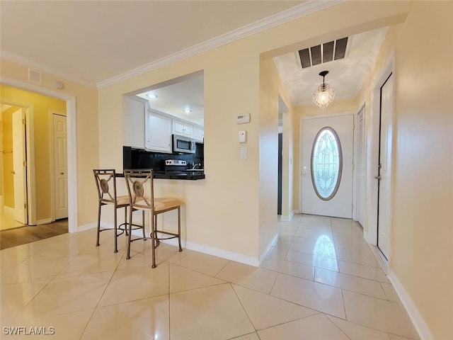 foyer entrance with ornamental molding, light tile patterned floors, and an inviting chandelier