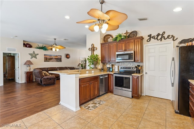 kitchen with light wood-type flooring, sink, kitchen peninsula, stainless steel appliances, and ceiling fan