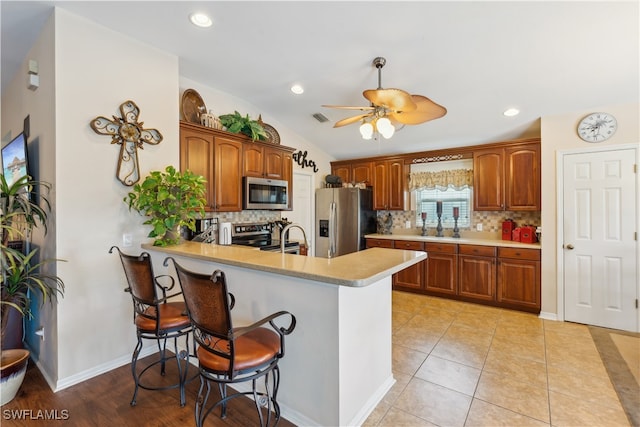 kitchen with a kitchen breakfast bar, kitchen peninsula, stainless steel appliances, lofted ceiling, and ceiling fan