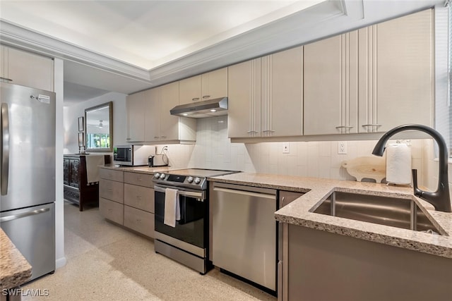 kitchen with appliances with stainless steel finishes, light stone counters, backsplash, cream cabinets, and sink