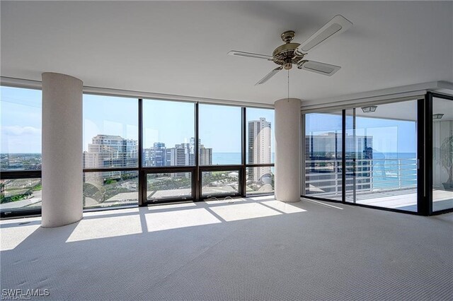 unfurnished room featuring ceiling fan, expansive windows, and a water view